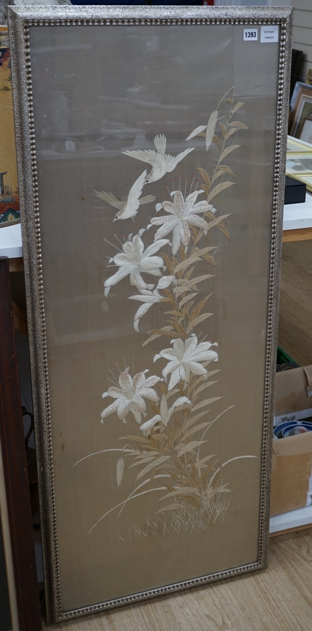A 1900 to 1920’s Japanese silk embroidery of birds in flight and flowers on a grey background, 131cm high, 52cm wide, together with a Japanese silk and metallic thread still life embroidery on black background, with couc